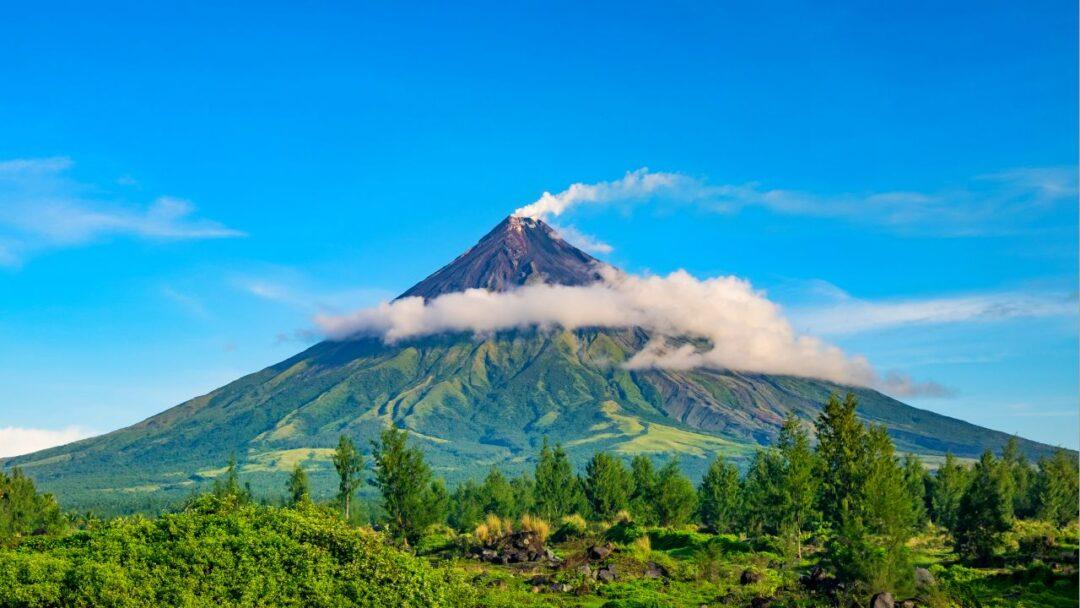 A serene green volcano standing tall against a clear blue sky, Exploring Volcanoes: Forces of Nature and Geological Wonders.